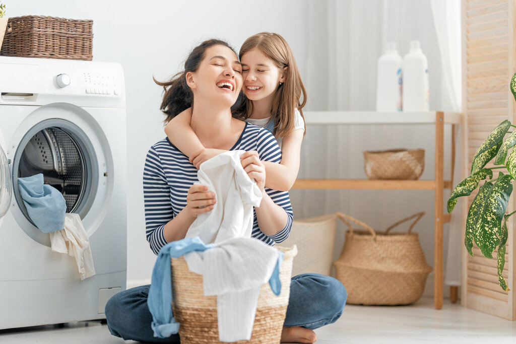Mutter und Tochter beim Wäschewaschen Junge Mutter und kleine Helferin haben Spaß beim Waschen zu Hause.