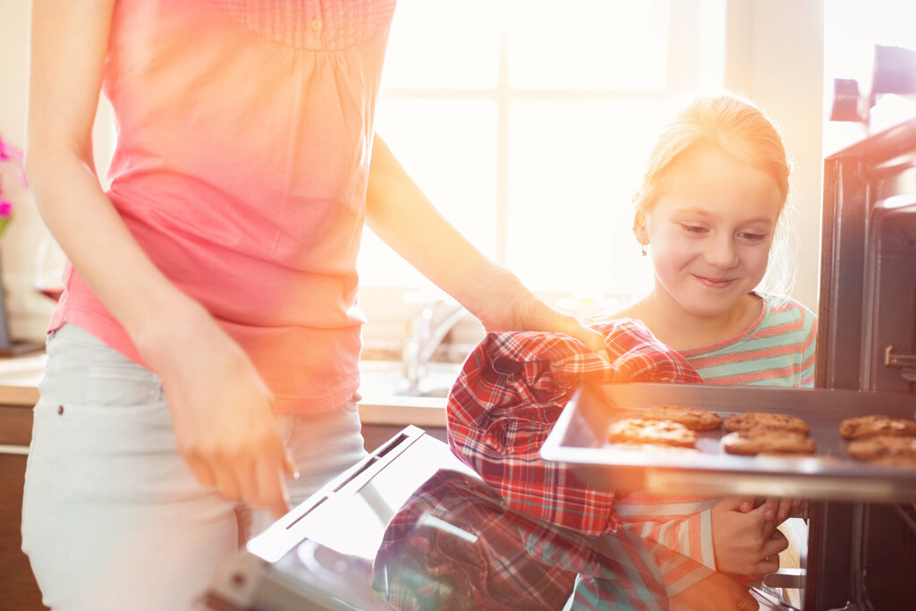 Mutter und Tochter backen gemeinsam Kekse Mutter entnimmt Plätzchen aus dem Backofen und Kind freut sich